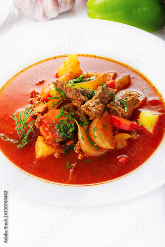 Hot beef hungarian goulash soup with paprika, beef, potatoes, carrots, onion, pepper and herbs. Ingredients for dish. White background. High key.