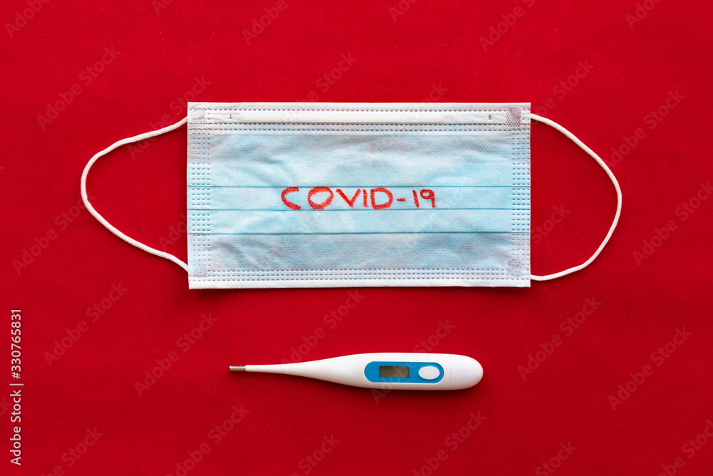 Protective face mask and thermometer on red background. Virus and disease protection concept. Novel coronavirus 2019-nCoV concept. Protective face mask and thermometer on red background. Virus and disease protection concept. Novel coronavirus 2019-nCoV concept.