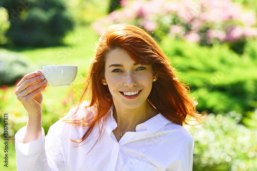 Konstfotografi Portrait of cute red haired young woman with cup coffee, outdoor