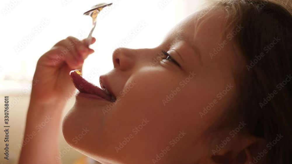 Little child girl eat honey as it drops on her tongue licking it out ...