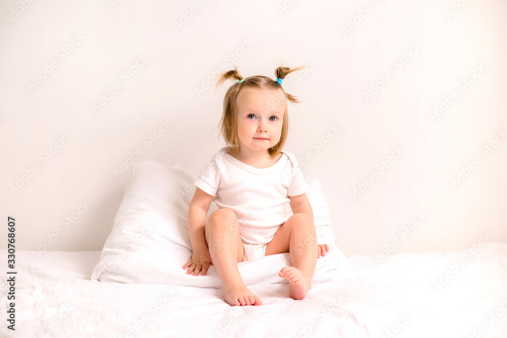 baby girl smiling in white clothes lying on a bed with white linens baby girl smiling in white clothes lying on a bed with white linens