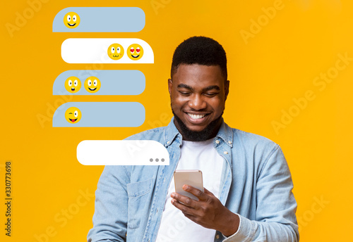 Millenial African American guy using smartphone for chat communication on orange background, empty space