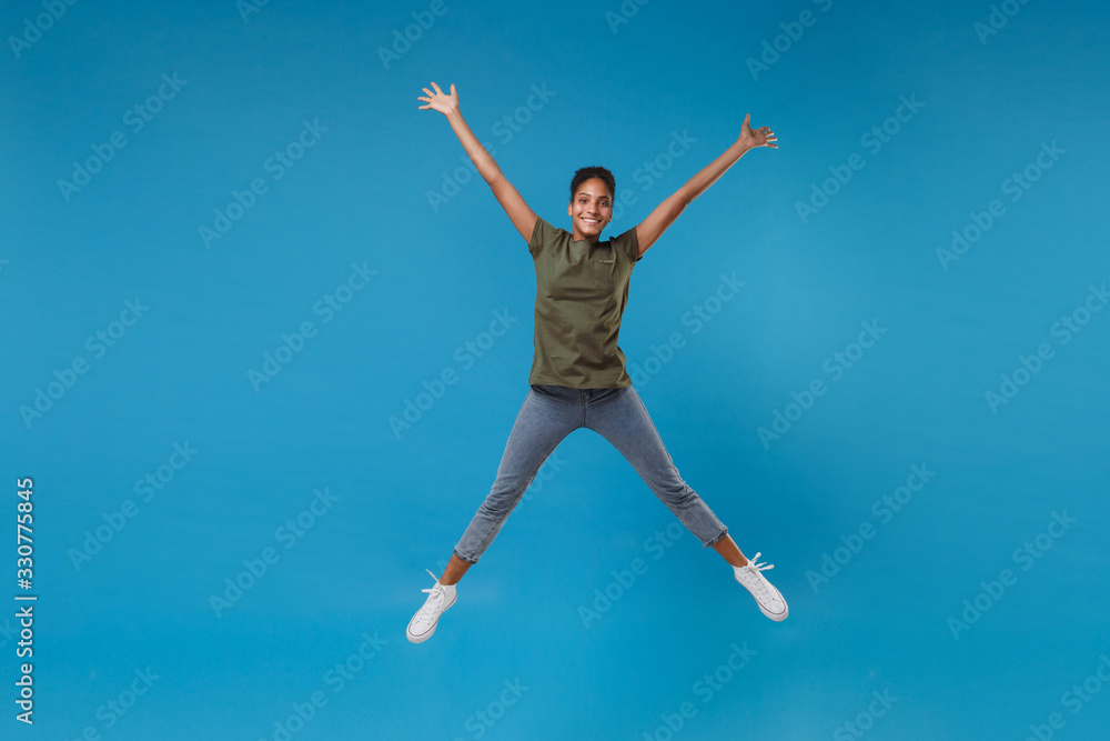 Funny young african american woman girl in casual clothes posing isolated on bright blue background studio portrait. People lifestyle concept. Mock up copy space. Jumping, spreading hands and legs.