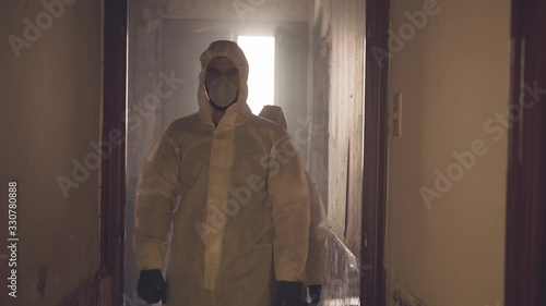 Slow motion video of two scientists wearing protective insulation suit inspecting and walking in a comprised broken house during a virus outbreak photo