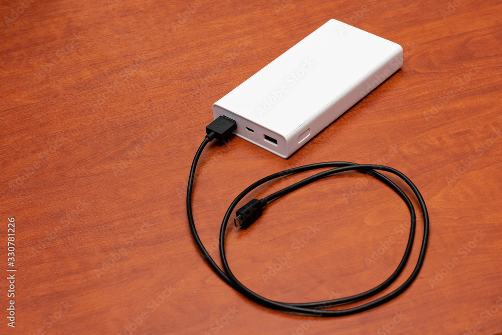 white powerbank with black cable on a wooden table background