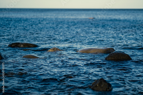 sunny beach with blue water and large rocks in the sand