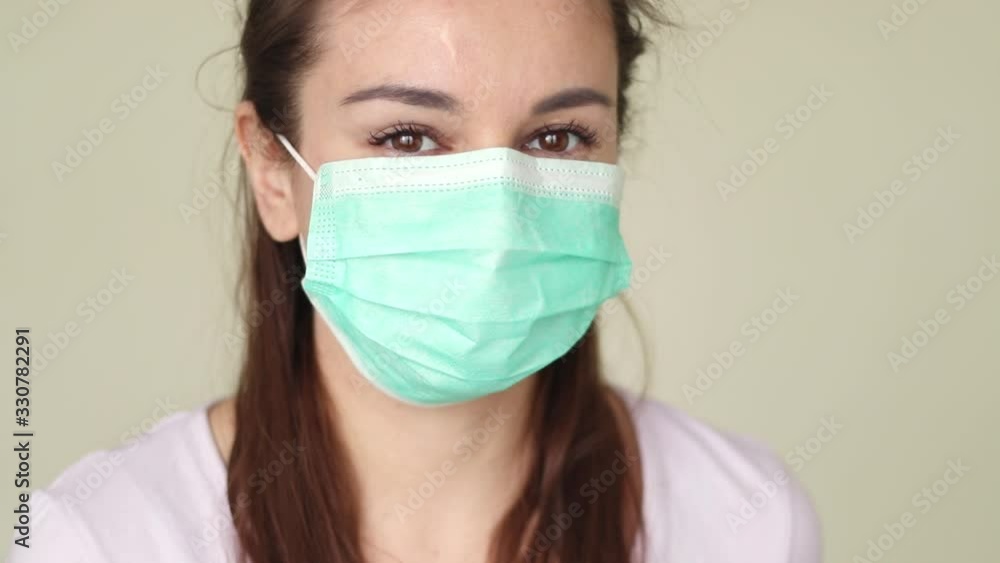 woman putting on surgical mask for corona virus prevention. Close-up of a young woman in a protective medical mask, she looks directly woman putting on surgical mask for corona virus prevention. Close-up of a young woman in a protective medical mask, she looks directly