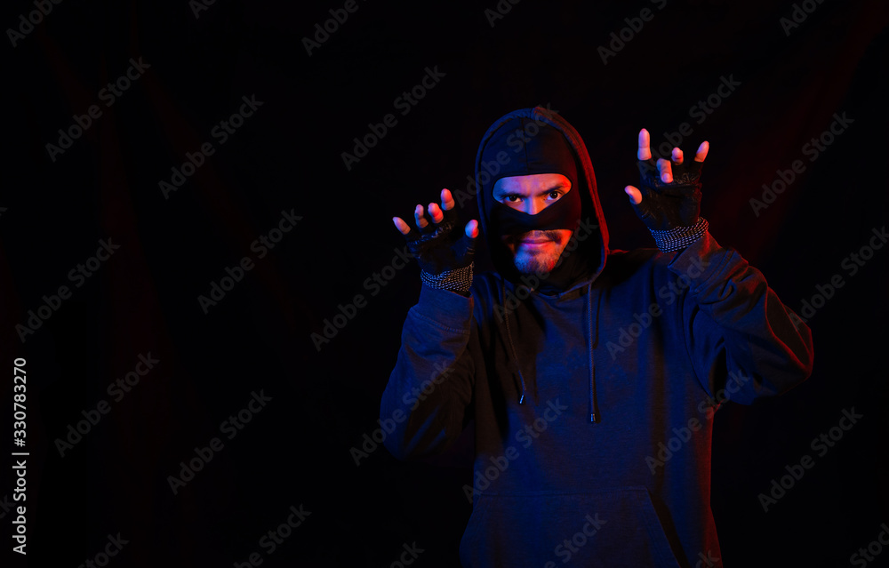 Robber, a thug in a balaclava raised his hands on a black background, surrenders. Robbery, hacker, crime, theft, arrest. Copy space Robber, a thug in a balaclava raised his hands on a black background, surrenders. Robbery, hacker, crime, theft, arrest. Copy space