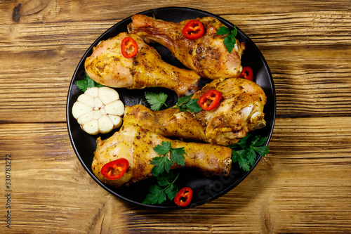 Roasted chicken drumsticks with spices in a black plate on a wooden table. Top view