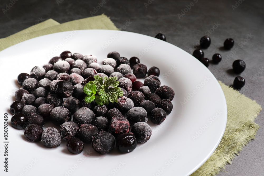 Frozen black rowan berries on a white plate and cement background. The concept of the use and preservation of frozen foods. Frozen black rowan berries on a white plate and cement background. The concept of the use and preservation of frozen foods.