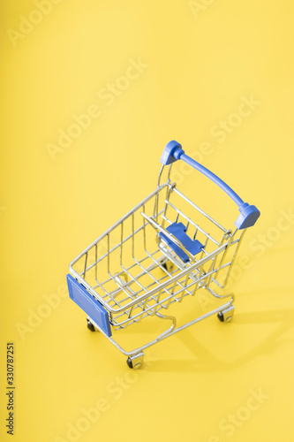 Close up of supermarket grocery push cart for shopping with black wheels and blue plastic elements on handle isolated on yellow background. Concept of shopping. Copy space for advertisement.