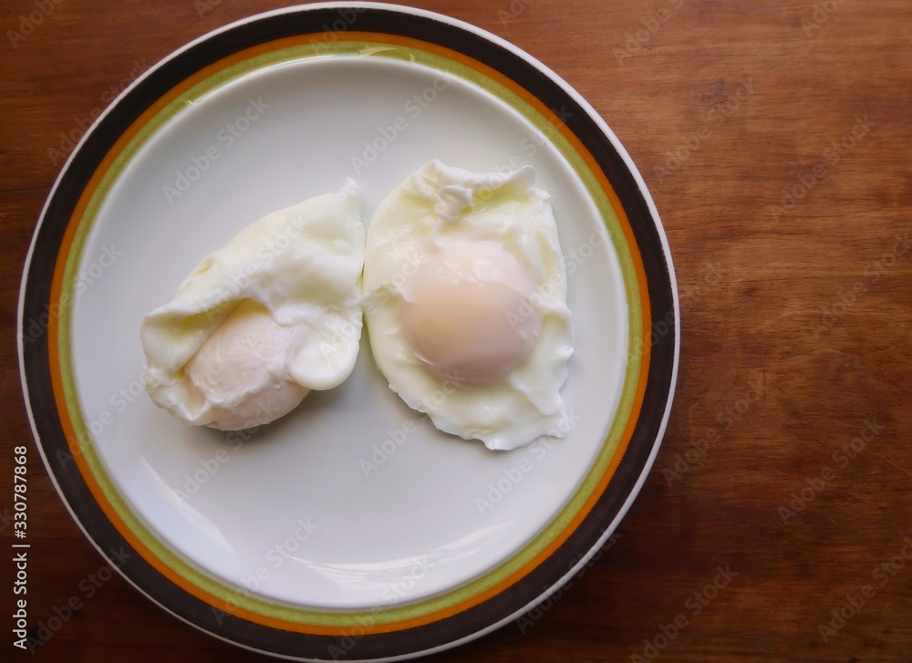 Top view of two freshly poached eggs served on a vintage plate on a wooden table. Top view of two freshly poached eggs served on a vintage plate on a wooden table.