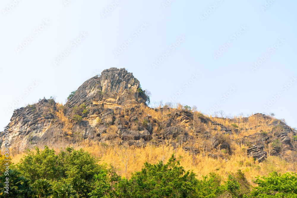 Limestone mountain peak At the bottom there is a yellow grass. And green trees With a beautiful sky Limestone mountain peak At the bottom there is a yellow grass. And green trees With a beautiful sky