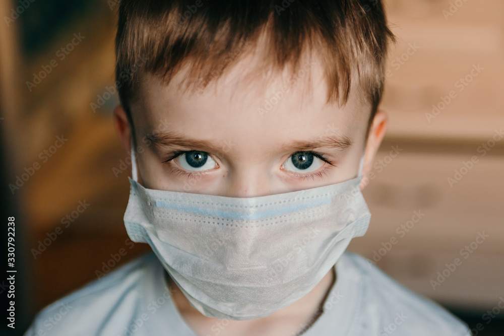 Close-up face of a boy with blue evil eyes in a protective blue medical mask covering his nose and mouth. Close-up face of a boy with blue evil eyes in a protective blue medical mask covering his nose and mouth.