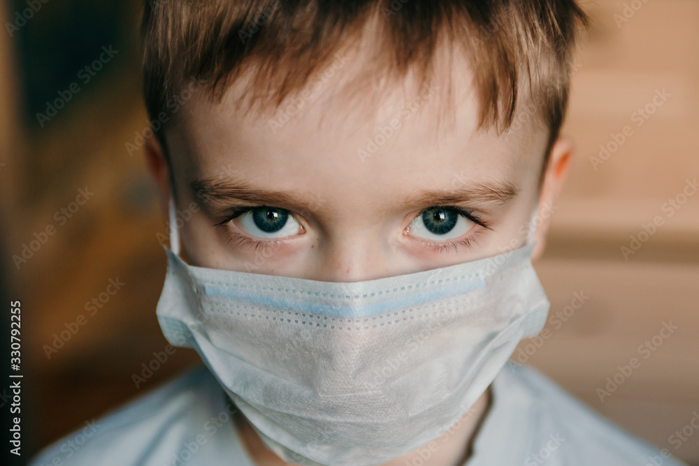 Close-up face of a boy with blue evil eyes in a protective blue medical mask covering his nose and mouth. Close-up face of a boy with blue evil eyes in a protective blue medical mask covering his nose and mouth.
