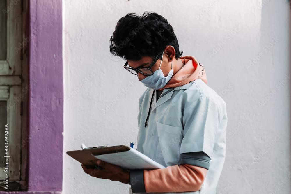 Fototapeta premium Closeup portrait of an Indian doctor writing on his examination pad during the Corona Virus pandemic