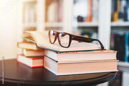 Glasses on stack of books. Library in the background. Books and glasses.