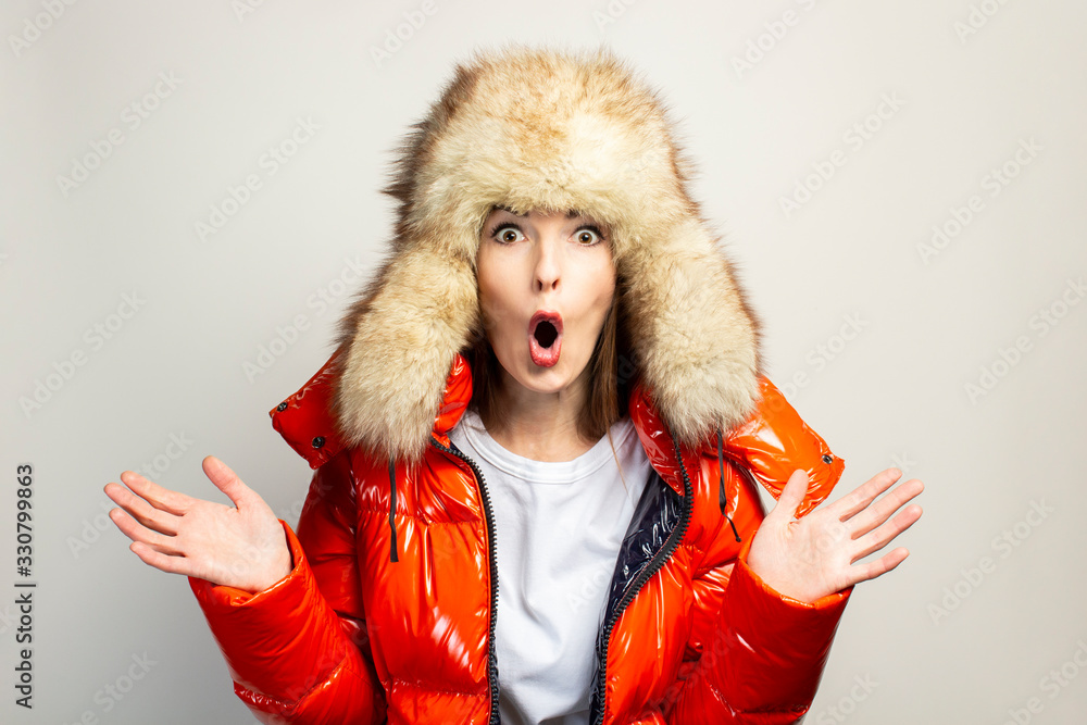 surprised young girl in a red jacket and a fur hat, looking at the camera in shock in front of him on a light background. Concept gestures, advertising, fashion surprised young girl in a red jacket and a fur hat, looking at the camera in shock in front of him on a light background. Concept gestures, advertising, fashion