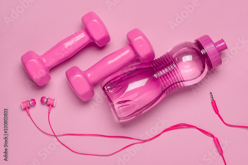 Dumbbells, bottle and headphones on pink background