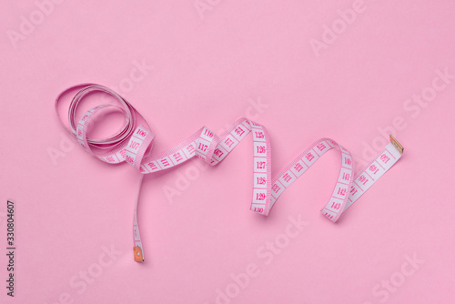 Measuring tape on pink background, top view