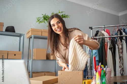 Young woman selling products online and packaging goods for shipping. Women, owener of small business packing product in boxes, preparing it for delivery photo