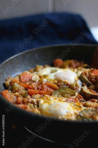 Shakshuka in a pan, with seasonal vegetables and eggs. Selective focus.