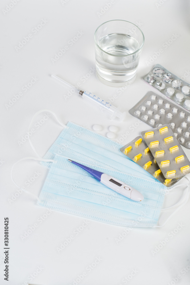 Tablets, capsules, medications, a thermometer and a syringe lie on a white background. Medical AIDS for fighting viruses, mask, coronavirus, covid 19 Tablets, capsules, medications, a thermometer and a syringe lie on a white background. Medical AIDS for fighting viruses, mask, coronavirus, covid 19