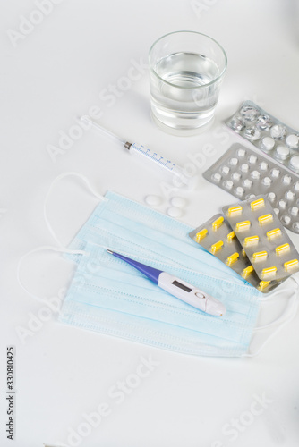 Tablets, capsules, medications, a thermometer and a syringe lie on a white background. Medical AIDS for fighting viruses, mask, coronavirus, covid 19
