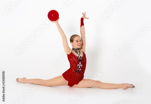 Obraz na plátně Cheerful female gymnast with ball sitting in leg split on white background
