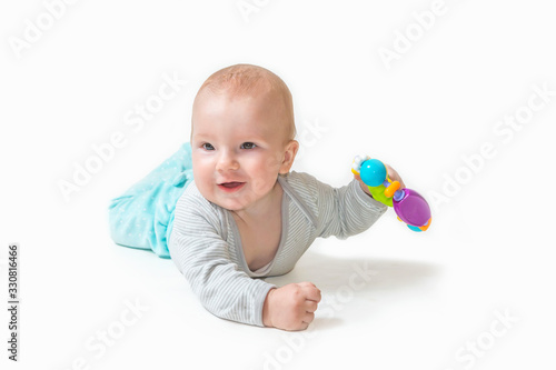 Playful little baby boy is lying and smiling at the camera, holding a toy in his hand.. All on the white background