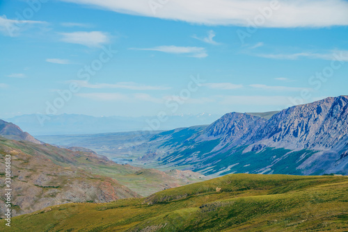 Beautiful aerial view to green hill and great mountains under blue sky. Long mountain range and long valley with forest. Awesome alpine landscape in sunny day. Vivid highland scenery on high altitude.