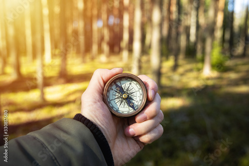 Compass in a hand with blurred trees background. Hiker searching direction with a compass in the forest. Copy space.