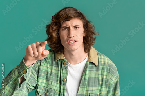 Frustrated teenager pointing finger at you in accusation on color background photo