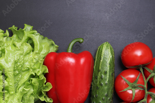 Fototapeta Naklejka Na Ścianę i Meble -  Green lettuce, red ripe tomatoes on a branch, fresh cucumbers and red bell peppers paprika. Vegetables on a black textured background.