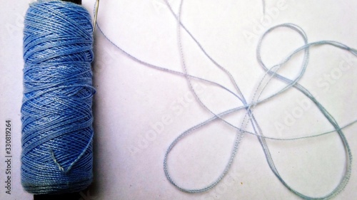 A close-up view of a blue thread spool with a needle against a white background.