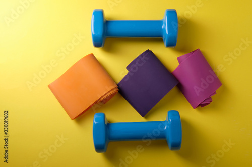 Multi-colored rubber bands for fitness on a yellow background, dumbbells