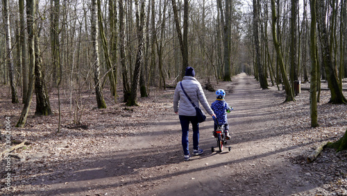 Dziecko na rowerze. Obok idzie mama. Rowerem po ścieżce rowerowej. Nauka jazdy na rowerze dziecięcym. Wycieczka do lasu z dzieckiem, dzień wolny od pracy. Wiosenny leśny krajobraz.