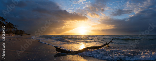 beautiful sunset over the sea, panorama view of a dramatic sunset with dark clouds. rain clouds or storm clouds before the storm, tree trunk lies in the water on the beach