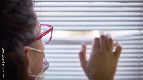 Girl with medical mask being diagnozed corona covid-19 virus look over window blinds. Female is hospitalized, put in carantine (isolation) to stop spreading  Coronavirus pandemic photo