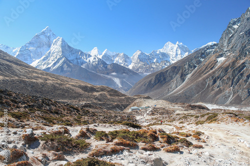 White snowy Ama Dablam mountain peak rises above mountain valley in Himalayas in the morning on the way to Everest base camp in Nepal. Clear blue sky. Theme of beautiful mountain landscapes.