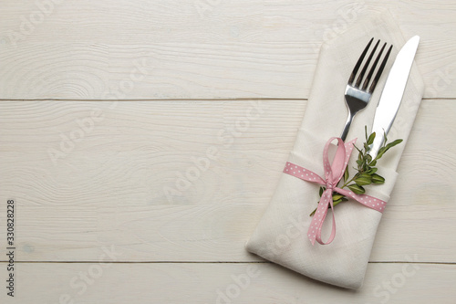 Table setting. Cutlery in a white napkin with a pink ribbon, fork and knife on a white wooden table. top view