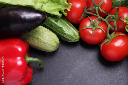Green lettuce, red ripe tomatoes on a branch, fresh cucumbers and red bell peppers paprika. Vegetables on a black textured background.