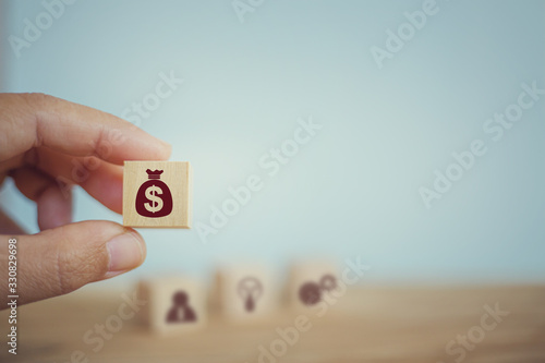Banking and finance, Financial planning concept: Hand chooses wooden cube blocks with US dollar bags icons. Management of corporate money To be consistent with the income in each quarter.