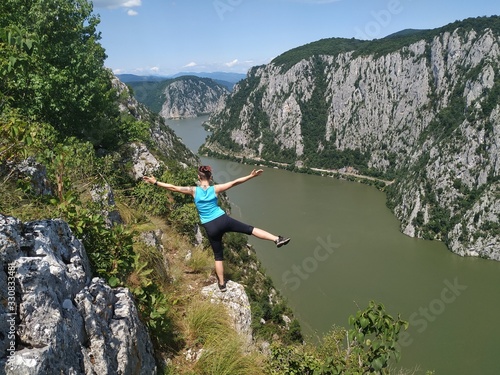 Girl standing on a rocky cliff hundred meters above the Danube Valley between Romania and Serbia  Yoga posing in the sun  meditating with arms wide open 