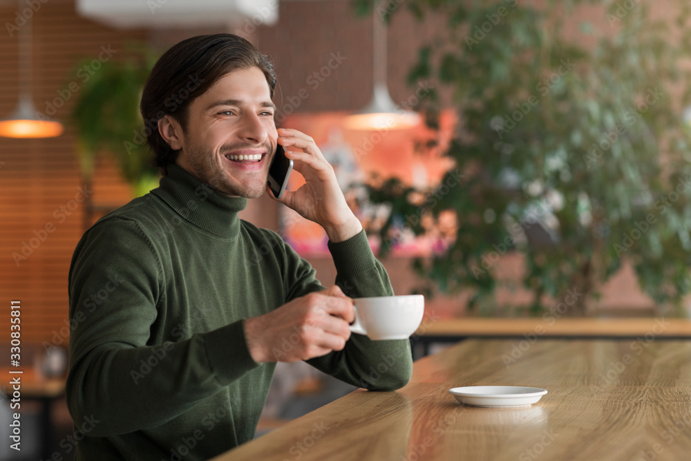 Young positive businessman drinking coffee while talking on phone Young positive businessman drinking coffee while talking on phone