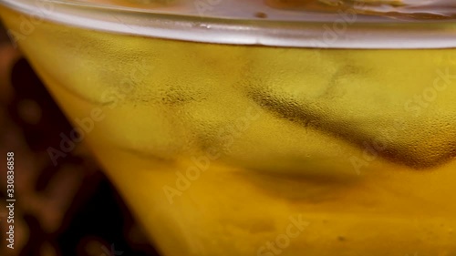 close up view of an alcoholic martini drink as it pans in frame. the ice begins to melt in the beverage cocktail.  the glass has condensation on the side from the booze being cooled 