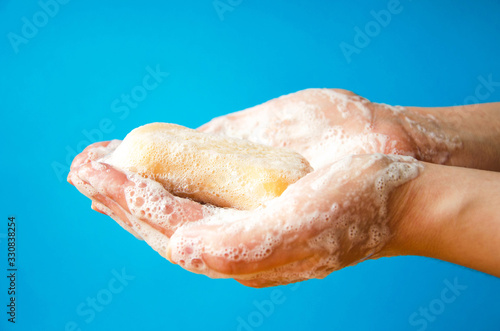 Women s hands are holding soap. Soap foam on the hands. Yellow soap in the hands. Woman washes soap with hands side view on a blue background. Virus protection.  COVID-19