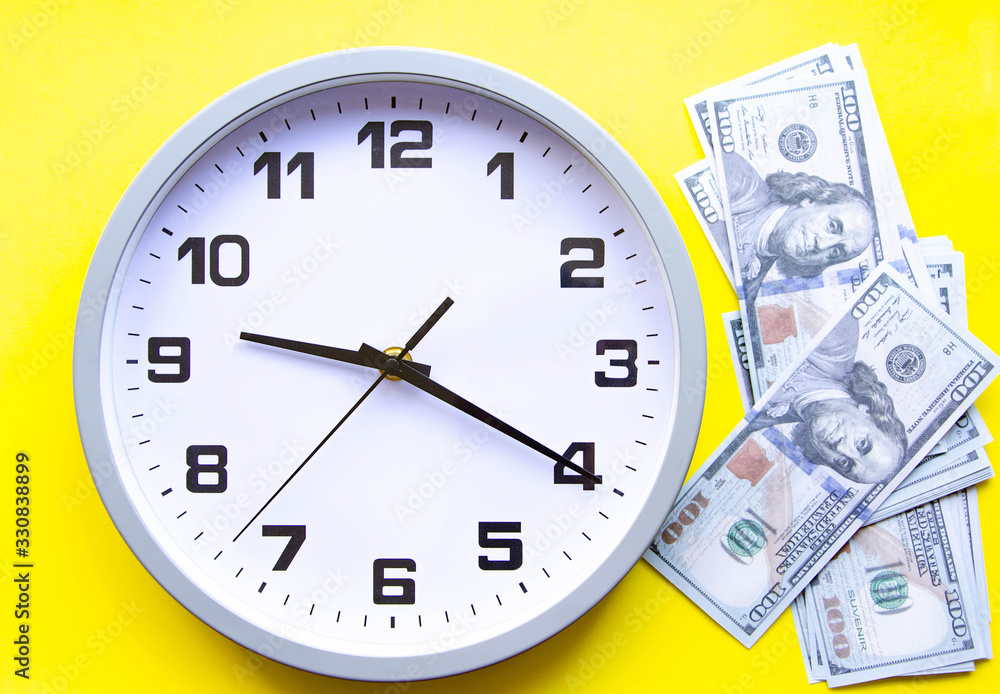 Analog white clock and dollars on a gray, yellow, blue background. Banknotes next to the clock, on top. Place for text. Business, are you ready? Copy Space Analog white clock and dollars on a gray, yellow, blue background. Banknotes next to the clock, on top. Place for text. Business, are you ready? Copy Space