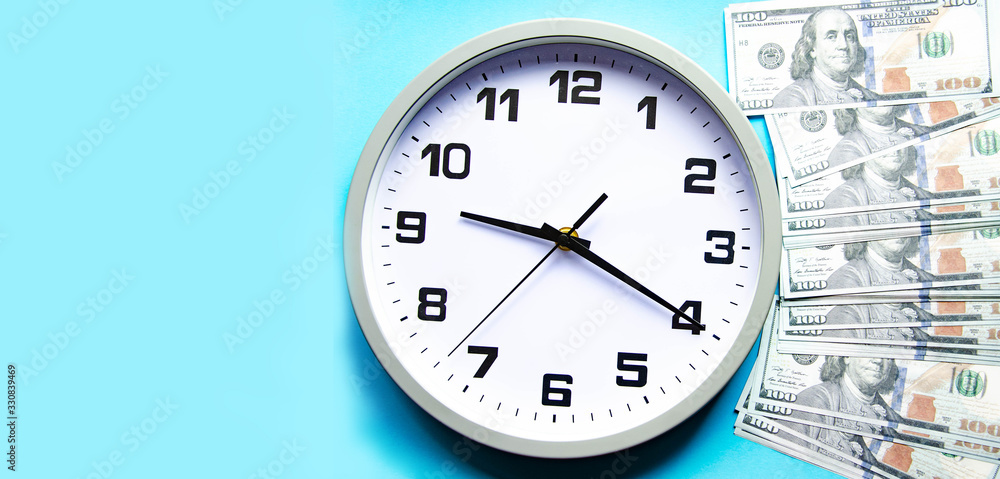 Analog white clock and dollars on a gray, yellow, blue background. Banknotes next to the clock, on top. Place for text. Business, are you ready? Copy Space Analog white clock and dollars on a gray, yellow, blue background. Banknotes next to the clock, on top. Place for text. Business, are you ready? Copy Space