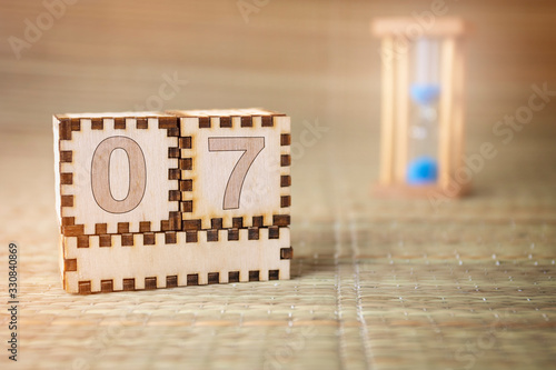 Calendar, wooden cube with date 7 and an empty space for the month, on an abstract woven hourglass background.